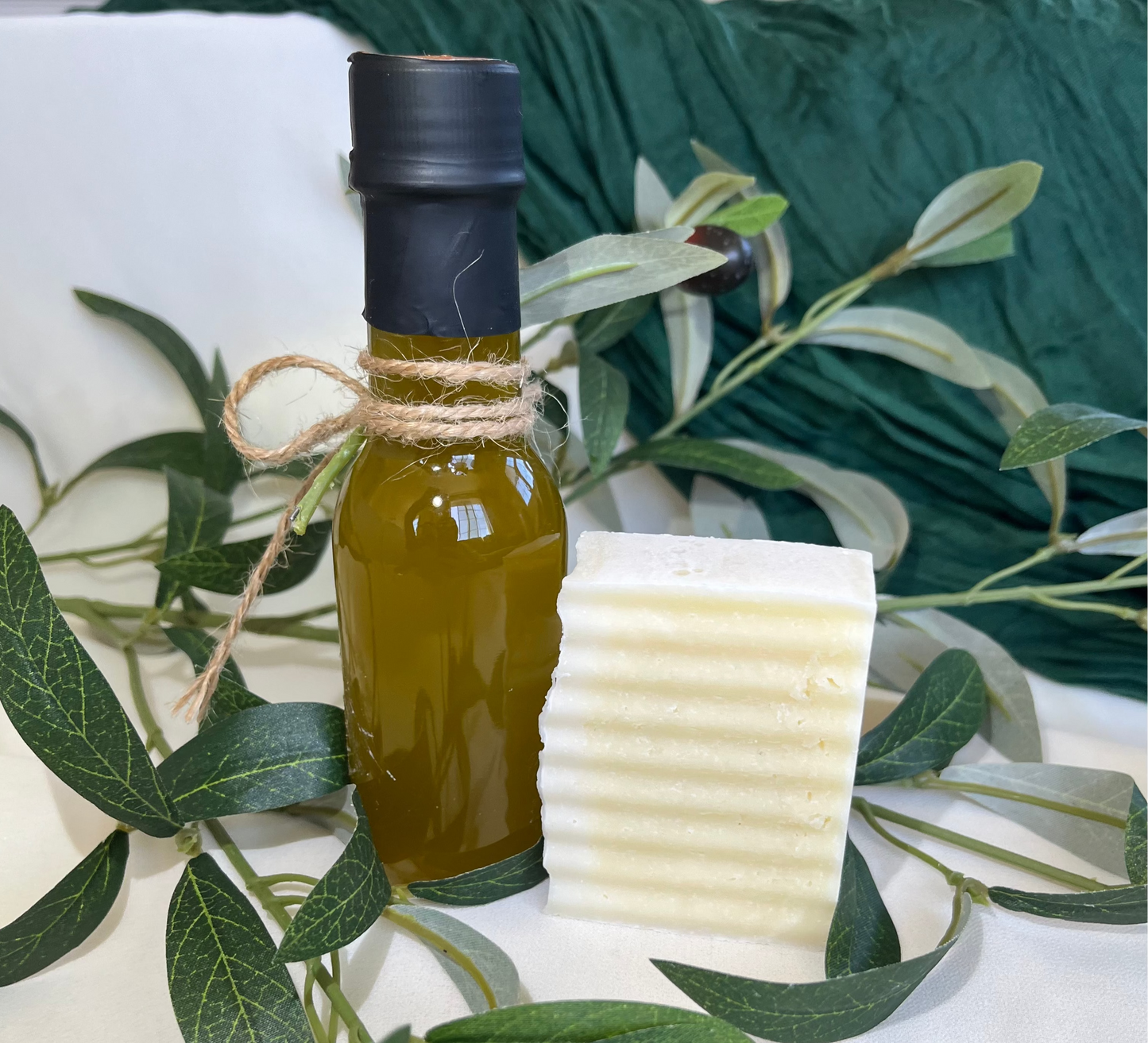 Bottle of olive oil and a block of soap with olive leaves on a white surface