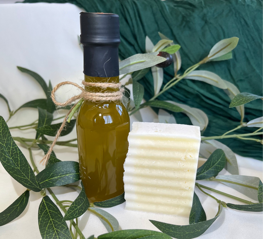 Bottle of olive oil and a block of soap with olive leaves on a white surface
